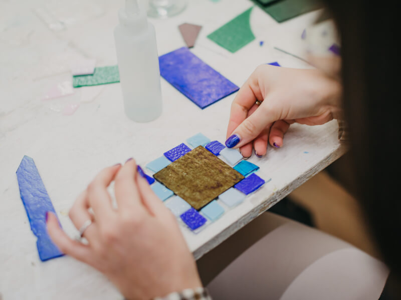 A woman is making fused glass art with blue glass fragments.